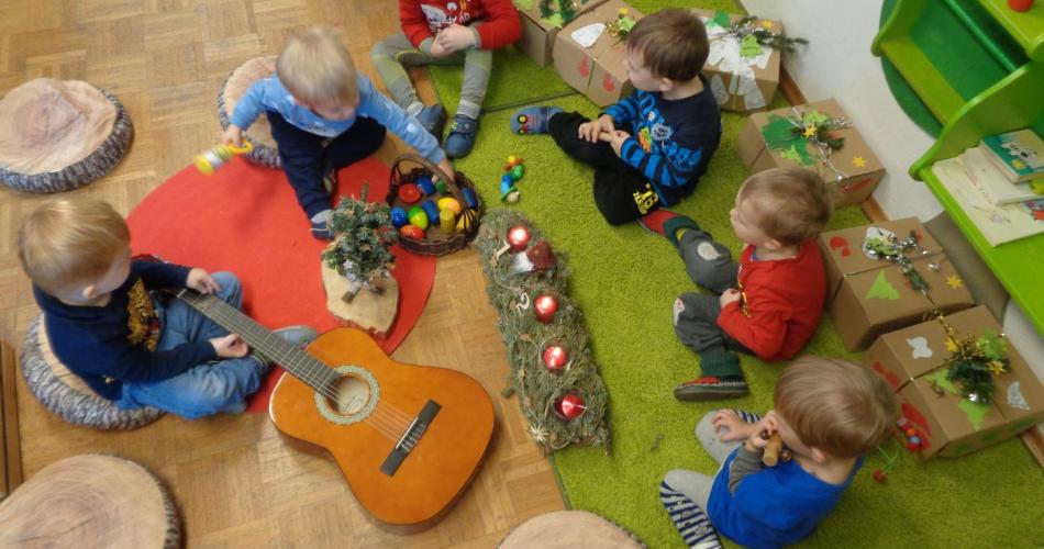 Kinder sitzen um den Kreis, Adventkranz, Gitarre und Geschenke